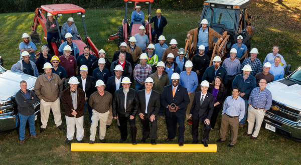 A group of people wearing hardhats and standing in a field looking up at the camera.