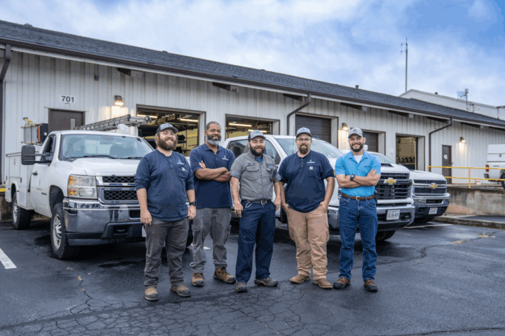 Five men standing in a parking lot in front of three work trucks