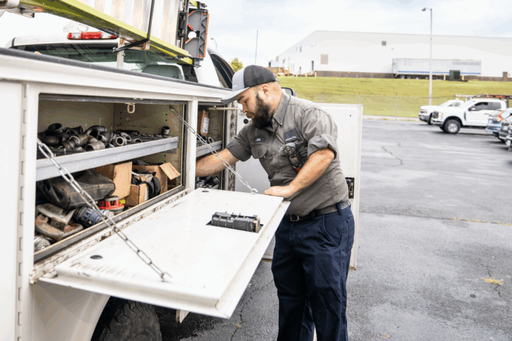 A man standing beside a work truck with the side storage panels open.